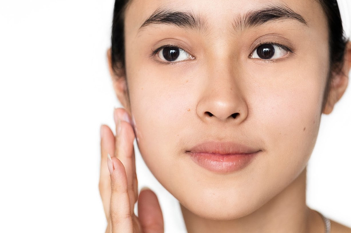 A close-up of a woman with smooth, radiant skin gently applying a whitening face cream to her cheek, highlighting clear complexion and healthy glow.