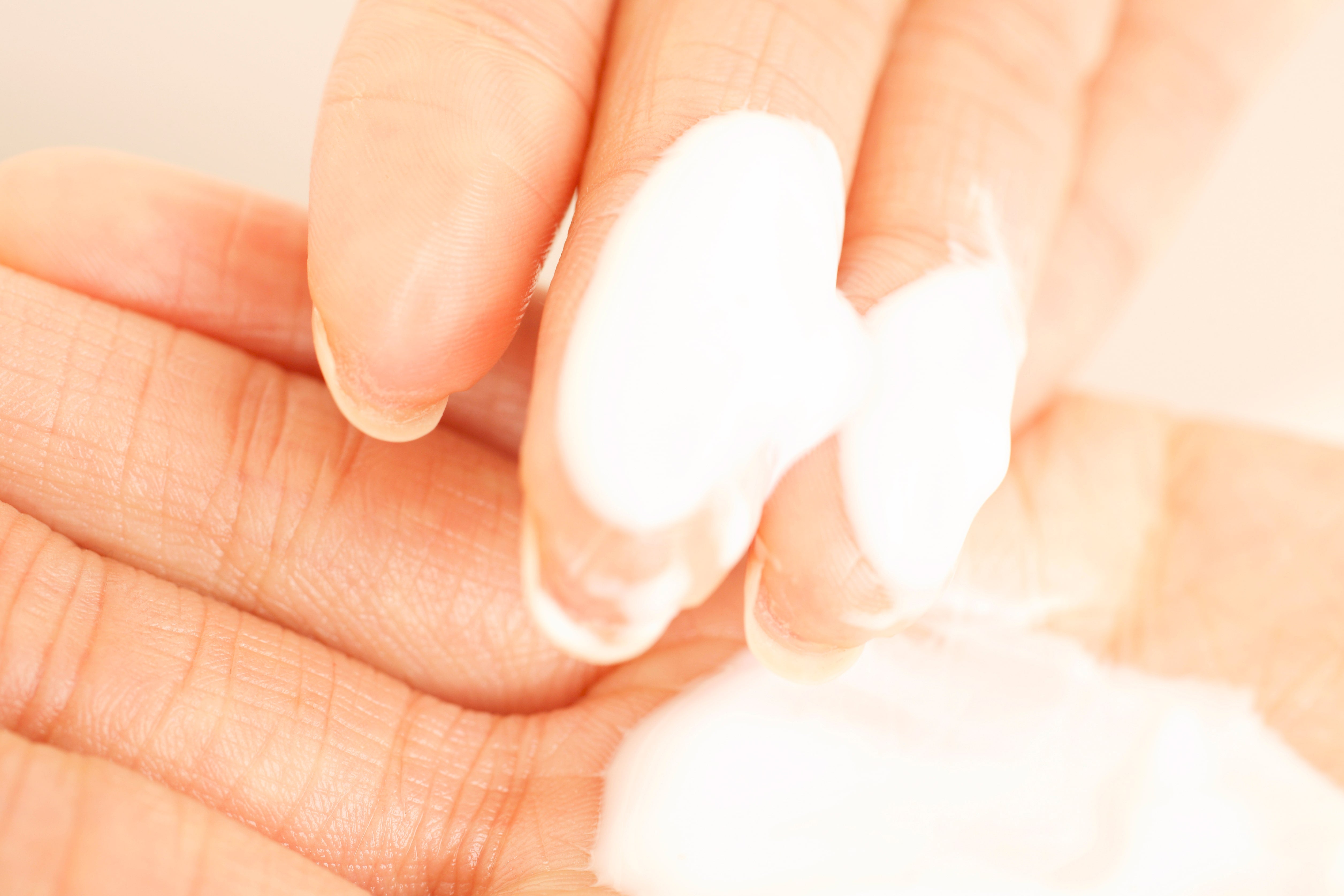 Close-up of fingers applying moisturizing cream on the palm as part of hand care tips.